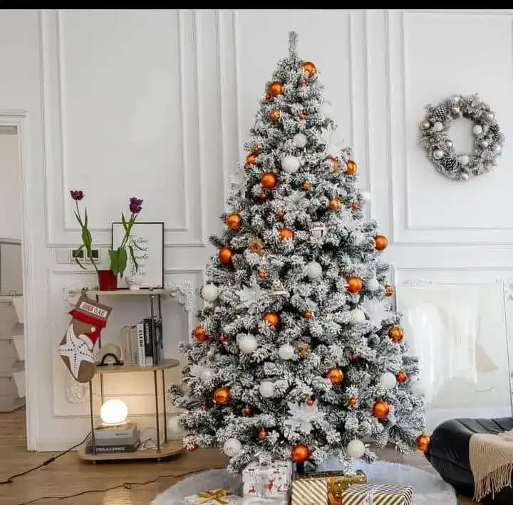 Brad artificial nins decorat cu globuri albe și portocalii, într-un living alb