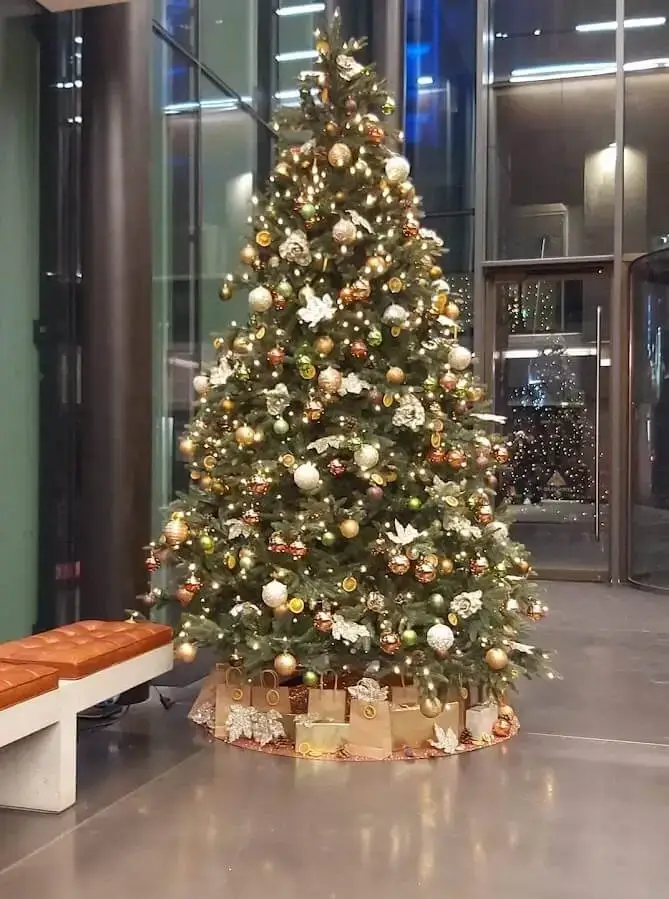 Brad artificial verde înalt, decorat cu globuri aurii, într-un hol modern